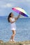 Curly girl in white sleeveless dress opens rainbow umbrella