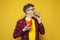 curly guy holds french fries and bites a big tasty burger on a yellow background, student eats fast food