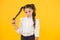 Curly hair ponytails for back to school. Adorable small girl twisting hair around her finger on yellow background. Cute