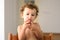 Curly-haired baby girl eats fruit sitting indoors at home in summer