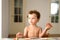 Curly-haired baby girl eats fruit sitting indoors at home in summer