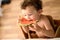 Curly-haired baby girl eats fruit sitting indoors at home in summer