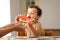 Curly-haired baby girl eats fruit sitting indoors at home in summer