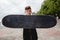 A curly-haired European teen holds a black old shabby skate in front of him. Only the skate is in focus. Space for text