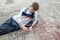 A curly-haired European tired teenager in a gray jumper is lying on the pavement leaning his elbow on a skate