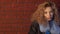 Curly haired young woman posing in front of brick wall