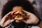 Curly hipster holding  craft mouth-watering bacon and angus beef burger flavored with crunchy fried onion, adding freshly cut pota