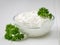 Curly leaves of parsley and a bowl of curd cream on a white wooden rustic table.