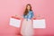 Curly long-haired girl with discontented face expression poses with bags from favorite clothing store. Fascinating young