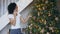 Curly mixed race girl decorating Christmas tree at home and chatting using smartphone