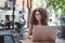 Curly Moroccan girl in eyeglasses with laptop in outdoor cafe