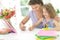 Curly schoolgirl with mother drawing at home