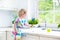 Curly toddler girl in colorful dress washing dishes