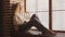 Curly young adult woman sitting under the window in loft apartment