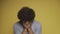 Curly young man sobs, covering his face with his hands. Filming in the studio on an isolated yellow background. High