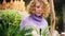 Curly young woman looking green plants and flowers in orangery. Florist woman in violet sweater touching plats indoor