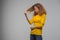 Curly young woman in yellow clothes displeased looking at hair o