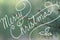 Cursive handwriting typography saying Merry Christmas on blurred blue spruce Christmas tree