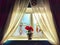 Curtains frame a sunlit window with vibrant red flowers on sill. Bright Morning Sunlight Through Window With Red Flowers