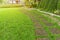Curve pattern walkway of square Laterite stepping stone on fresh green grass yard, smooth carpet lawn, brown gravel and concrete