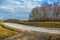 Curve road in autumn with green meadow and blue cloudy sky and sun. Empty curved road at sunny day. Country land and journey.