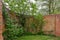 Curved ancient red brick wall with trees and shrubs growing beside it