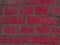 Curved brickwork of bright pink crimson geometric horizontal bricks bonded with grey cement grout between square stones