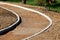 Curved concrete curb at local sidewalk construction site filled with gravel and small grain sand surrounded with grass and trees