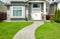 Curved concrete pathway over green lawn to the main entrance of small house