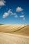 Curved lines of a ploughed field with a blue sky and white fluffy clouds of the rolling farmland in Sussex, England, UK