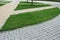 curved pedestrian pavement of stone tiles in park with slope landscape lighting and green plants on flower bed, meadow of on turf