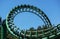 Curved Rollercoaster at a theme or amusement park empty green metal tracks and on blue sky background.