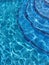 Curved steps into swimming pool, view from above through water on blue mosaic tiles. Distortion. Refraction. Vertical orientation