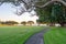 Curving concrete path leading under shady pohutukawa trees to waterfront at sunrise