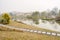 Curving waterside path on withered lawn in light winter mist