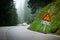 Curvy mountain road with slippery route sign and blurred white car in the background