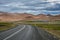 Curvy road, empty meadow and red mountains in the background in Myvatn region, overcast day in summe