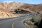 Curvy sandy road on a highway that runs along the Dead Sea from one side and Edom Mountains at Arava Desert from the other in