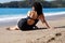 Curvy woman in black swimsuit sitting on the sea beach, rear view