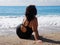 Curvy woman in black swimsuit sitting on the sea beach, rear view