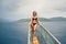Curvy woman in a red swimsuit standing on the front of the boat deck on turqouise blue sea background. View from the