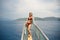 Curvy woman in a red swimsuit standing on the front of the boat deck on turqouise blue sea background. View from the