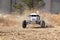 Custom single seater rally buggy kicking up trail of dust on san