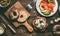 Cut in half bagel bun on wooden gutting board with bread knife and sandwich ingredients: salmon, avocado, hummus and quail eggs