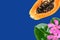 Cut in half ripe juicy papaya fuchsia pink exotic flowers on classic blue background. Tropical fruits summer vacation