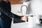 Cut view of man in black clothes hold electric kettle in hand. Water pours from tap. White smart kettle for heating