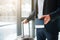 Cut view of man in suit stand at window in airport. He hold passport with ticket in it and suitcase with another hand.