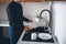 Cut view of young businessman in black clothes washing dishes alone in kitchen. Stand at sink and rub them with yellow