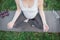 Cut view of young pegnant woman sitting in lotus pose in park alone. She meditate on yoga mate. Violet dumbells and