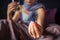 Cut view of young woman sits on bed and shows medicine in hand. It is blue capsule. There is glass of water in another